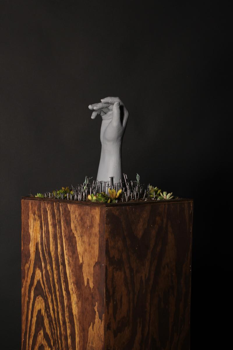 plaster hand, succulents and nails on wooden pedestal