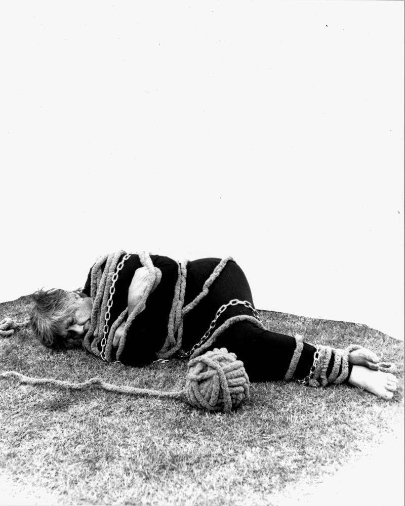 figure lying on ground wrapped in chains