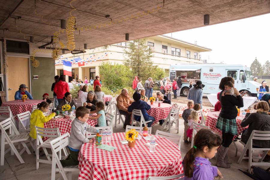 People sitting at outdoor tables with food trucks, crafts, and activities.