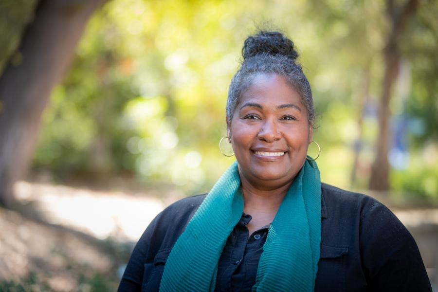 Wendy Jackson outside at Westmont smiling wearing a blue scarf and black shirt with her hair in a bun